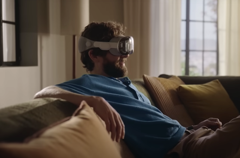 Mann sitzt auf Sofa und trägt die Apple Vision Pro VR-Brille in weiß